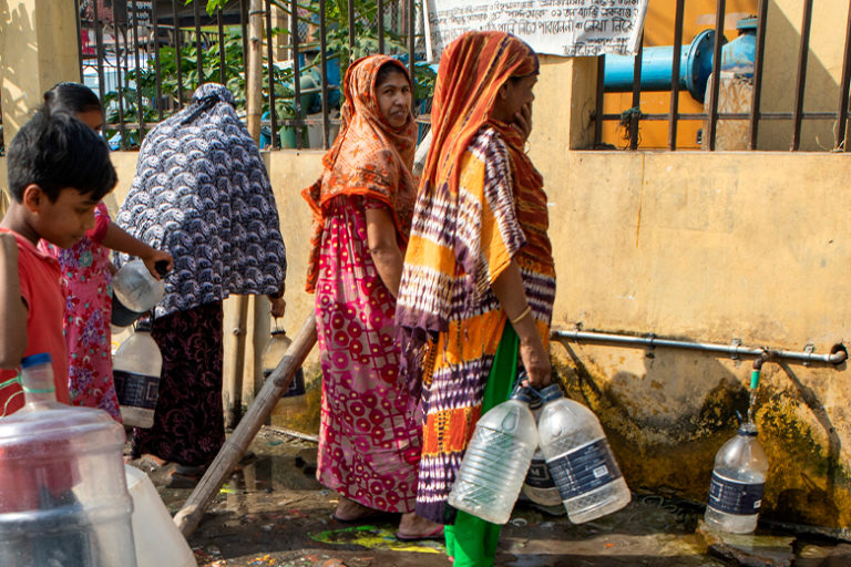 People line up to collect water from a community tap.