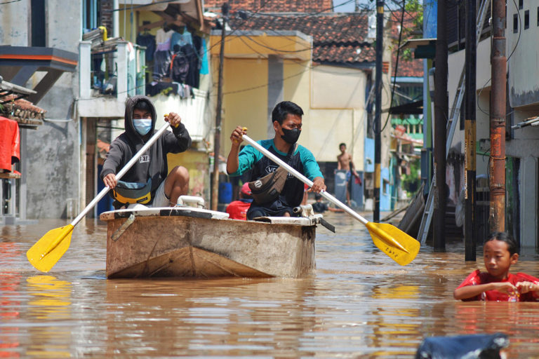 Residents paddle a boat down a flooded street in Bojongasih village.