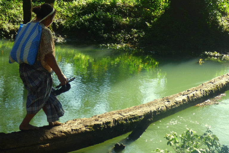 An Indigenous woman crossing a river. Image by Alicia MucúChoc/FAO.